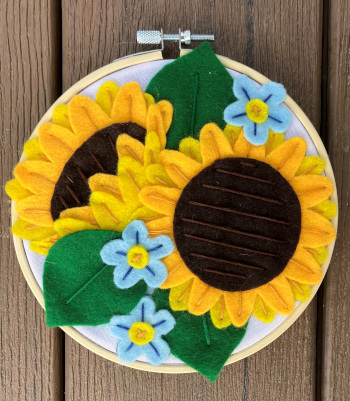 Two felt sunflowers stitched on an embroidery hoop with green leaves and small blue flowers