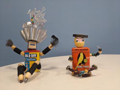 Two robot-like figures made from found objects, including an Old Bay tin, blocks, beads, metal objects