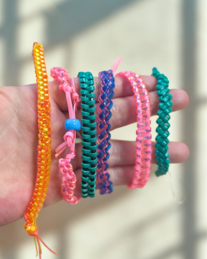 An array of brightly colored bracelets and keychains created with plastic craft string and woven into different patterns
