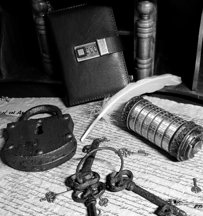 A black and white photo of a locked journal, large feather quill, cryptex, assortment of keys, and large metal lock, arranged clockwise on a background of handwritten old papers