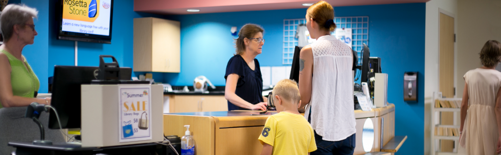 woman and boy standing at the checkout desk with two library staff members behind the desk