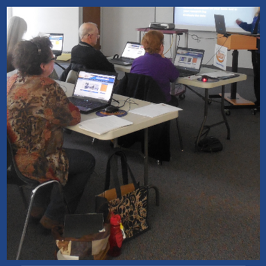 a group of adults in a classroom setting with computers in front of them