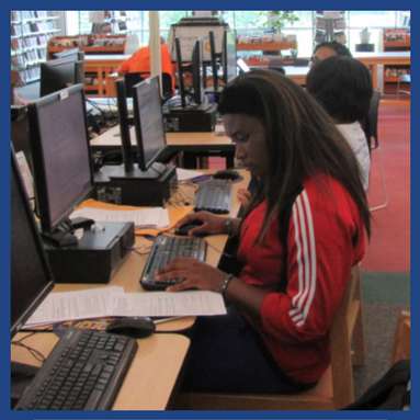 young woman sitting at computers with paper next to her