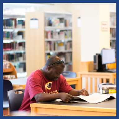 African American man in red shirt sitting at table reading newspaper