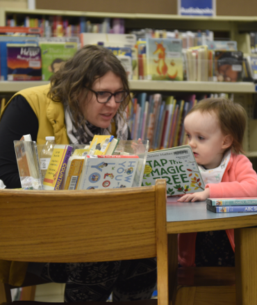 Mother and child sitting at a table reading a board book 