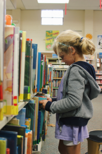 Girl in grey sweatshirt browsing library shelves