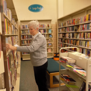 woman looking at book shelves with a cart of books behind her