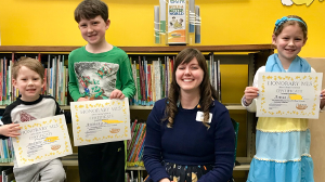 three children holding certificates and a librarian in the middle