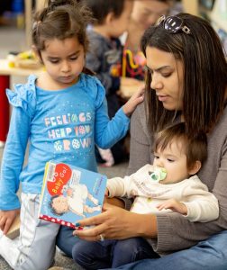 woman reading to an infant and a preschooler