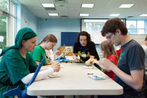 a group of teens sitting at a table doing a craft