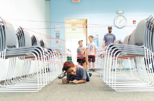 a child crawling under yarn tied between two sets of chairs