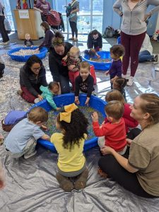 group of young children and adults surrounding a small pool filled with water beads