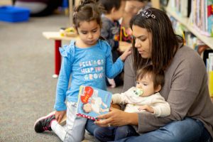 a mother and two children sitting on the floor reading a book