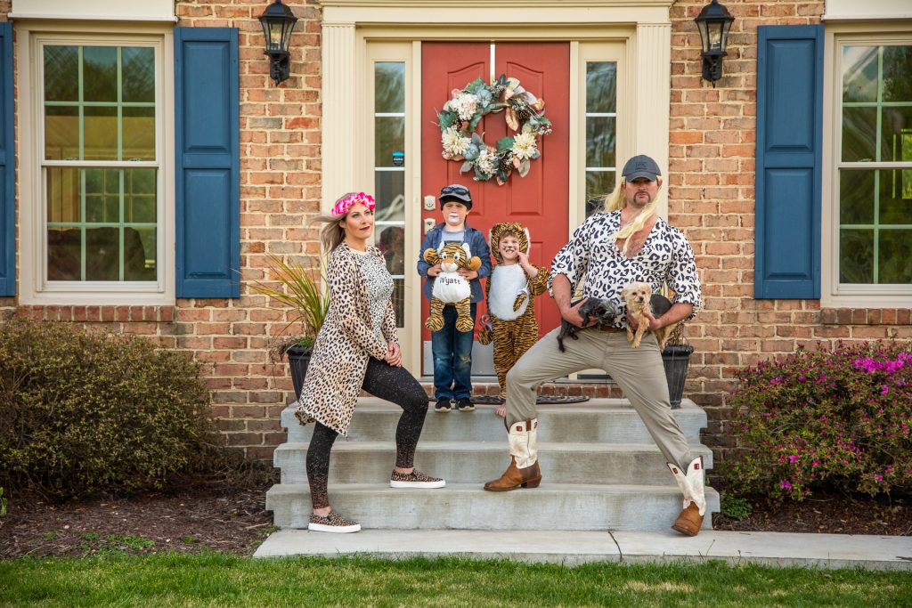 a mother, father, and two young boys stand on their front porch dressed in animal print and holding dogs and stuffed tigers