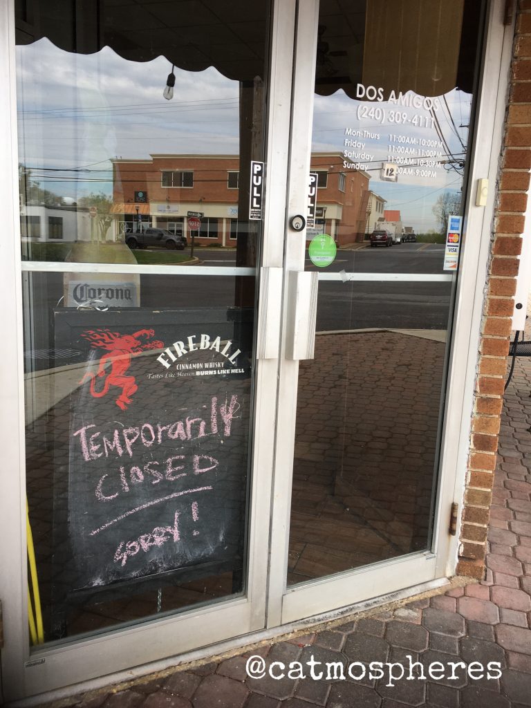 photo of a restaurant store with a temporarily closed sign and a cardboard Corona Beer bottle hiding behind the sign