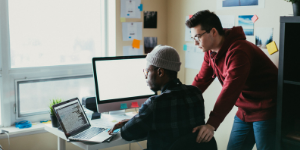 two men in front of a laptop and a computer monitor