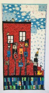 quilted scene of a brick building with birdhouses in front of it