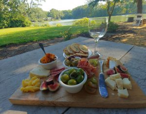 Charcuterie board and wine glass on a table next to a body of water