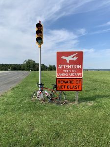 A traffic light with a bicycle leaning against it, two signs reading Attention, yield to landing aircraft and Beware of jet blast