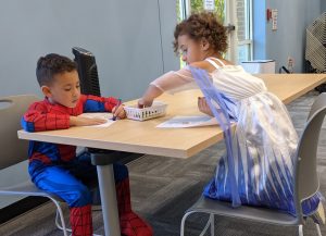 Young boy dressed as spiderman and a young girl in a blue dress playing at a table