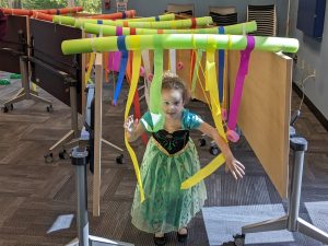 Young girl in a green dress moves through an obstacle course made of pool noodles and streamers
