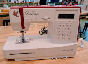 A white sewing machine with a pink top that says EverSewn and has a bird flying next to the logo