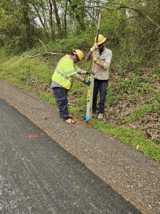 Two men in hard hats install a post in the ground