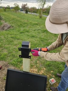 A woman in a hat installs a sign post