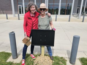 Two women stand in front of a sign post