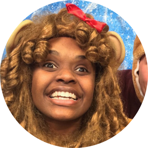 A Black woman wearing a lion's mane and ears smiles at the camera