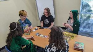 A group of five teens sitting around a table playing a card game