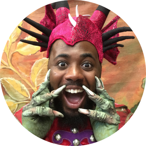 A grinning Black man wearing a bright pink & green dinosaur costume