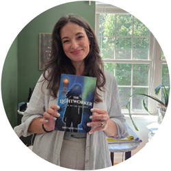 Abbie Richey Butler stands in front of a window holding her book, The Lightworker