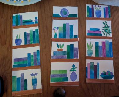 Three vertical pieces of art made from cut paper in the shape of books, plants, and other decor in shades of blue and green