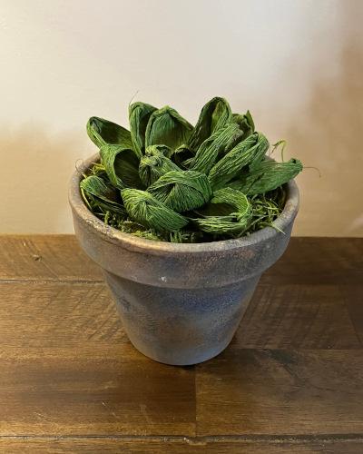 A blue painted terracotta pot with green crepe paper leaves and grass