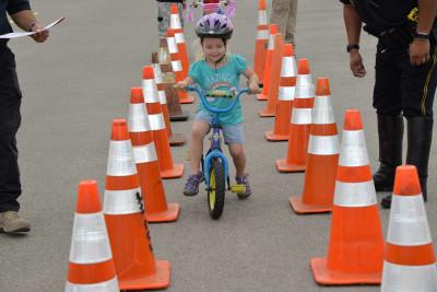 A young girl wearing a bike helmet and a blue shirt rides a bike between two lanes of orange traffic cones