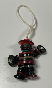 A keychain of a human figure made from green, brown, and black buttons