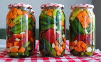 Three glass jars filled with multicolored vegetables, sitting on a red and white checkered tablecloth