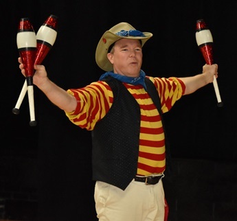 Man in a red and yellow striped shirt, hat, and vest, holding three bowling pins