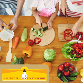 Overhead view of three people standing at a countertop cutting vegetables on cutting boards. The Healthy St. Mary's Partnership logo is in the bottom left.