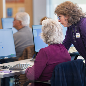 Woman sitting at a computer and another woman standing behind her, looking at the screen