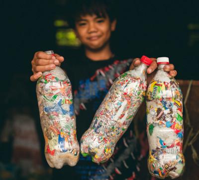 A young boy holds three 2 liter plastic bottles stuffed with plastic