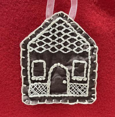 An embroidered gingerbread house ornament on a red background