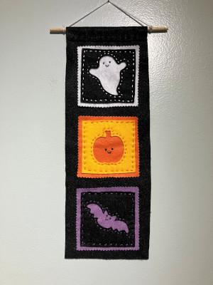 A Halloween banner made of felt featuring a ghost, pumpkin, and bat