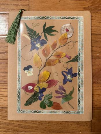A journal decorated with pressed flowers and plants and a tassel page marker