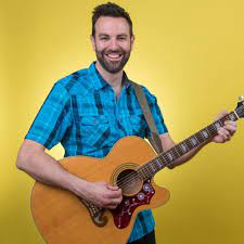 Mr. Jon, holding a guitar and smiling