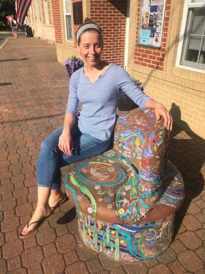 A woman in a blue shirt and jeans sits on a painted stone bench