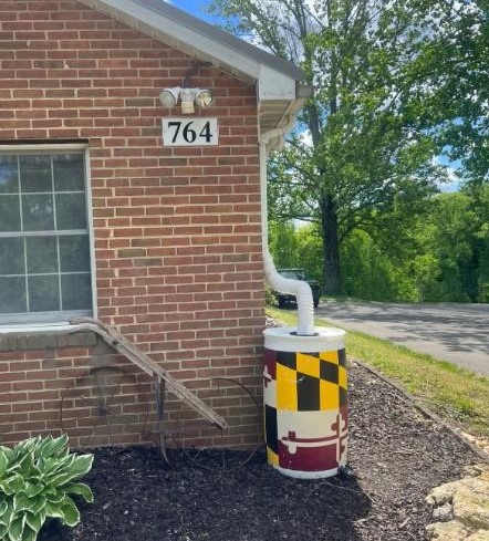 A brick house with a rain barrel painted with the Maryland flag attached to a downspout