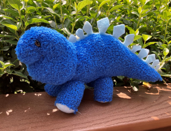 blue plush dinosaur with light blue spikes in front of greenery