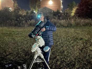 young person using a Celestron NexStar SE telescope mounted on a tripod during nighttime stargazing